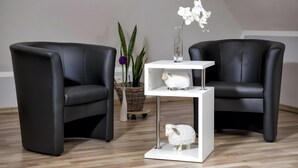 Two black leather chairs, a white side table with a glass shelf, a white sheep figurine, a white orchid, and a wicker basket with plants. - Apartment 'Schwälbchen' with Shared Garden and Wi-Fi (Fuhlendorf)