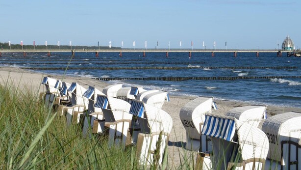 Beach chairs lined up on the shore, a pier with flags, and a dome structure in the distance. - Apartment 'Schwälbchen' with Shared Garden and Wi-Fi (Fuhlendorf)