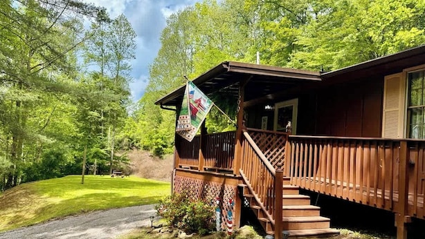 Une cabane en bois dotée d’un porche et d’un escalier menant à une porte, le tout entouré d’une végétation luxuriante.
