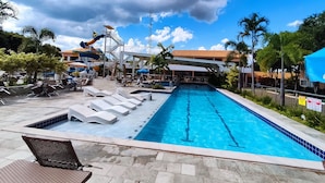 Zona de piscina con sillas de descanso, tobogán de agua y área de estar cubierta.