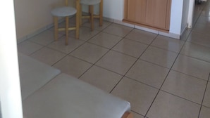 Una pequeña cocina americana con un mueble de madera, dos taburetes y una encimera blanca.