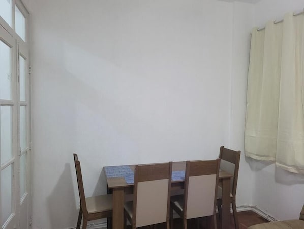Une pièce avec une table et des chaises en bois, une fenêtre aux cadres blancs et un rideau sur le côté droit.