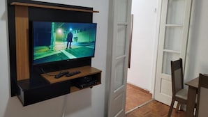 A TV mounted on a wall with a wooden shelf below, a door with a glass panel, and a chair in the room. - SUH Botafogo 03 Great Bars and Shopping (Rio de Janeiro)