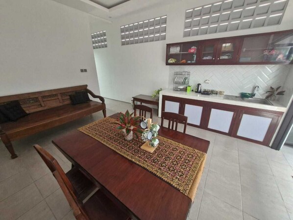 A dining area with a wooden table, chairs, and a bench. There is a kitchen area with cabinets and a countertop.