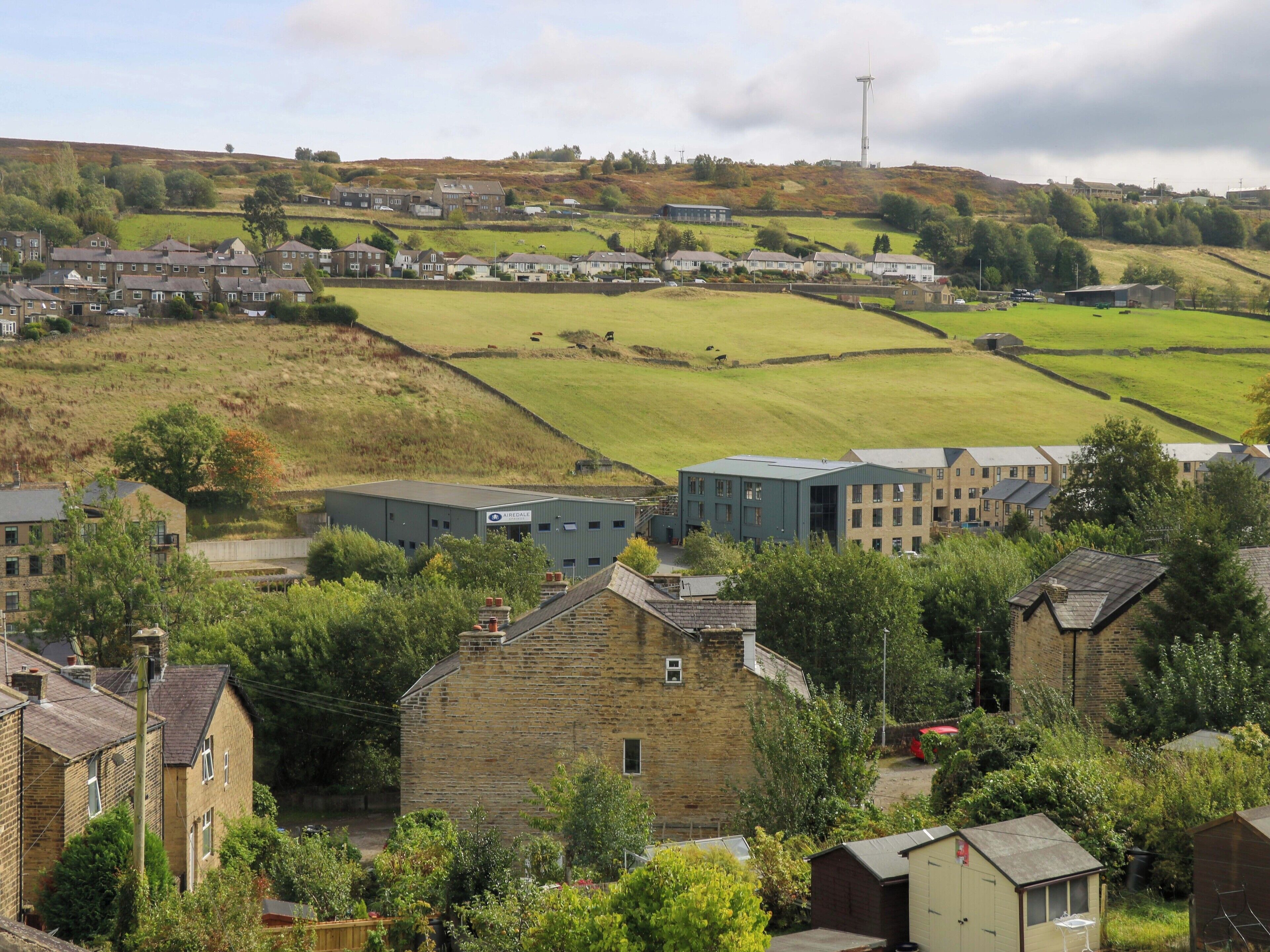 A residential area with stone houses, a modern building, and a wind turbine in the background.