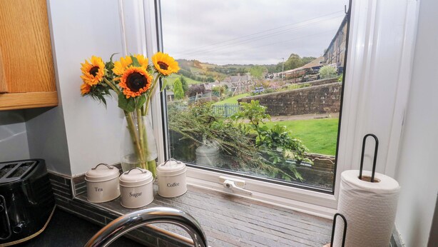 Una cocina con vista al río, un jarrón con girasoles y utensilios de cocina en el alféizar.