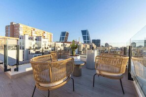 A rooftop terrace with wicker furniture, a potted plant, and a clear view of the cityscape. - Student Only Plaza Castilla (Madrid)