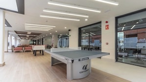Ein Pingpongtisch in einem modernen Innenraum mit klarem, minimalistischem Design, der eine Decke mit linearer Beleuchtung und eine Glaswand zeigt, die das Exterior reflektiert.