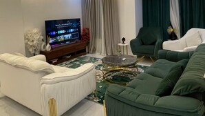 Ein modernes Wohnzimmer mit Fernseher, grünen und weißen Sofas, einem Couchtisch und einer Zierpflanze.