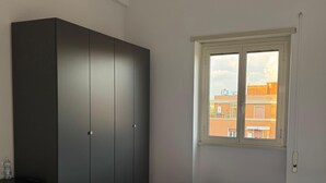 A bedroom with a bed, a wardrobe, a ceiling fan, and a window with a view of buildings. - The Monteverde Penthouse (Roma)