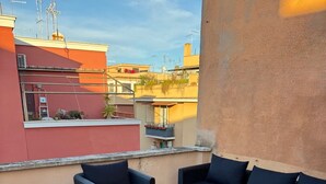 A rooftop patio with wicker furniture and a small table, surrounded by a low wall and a view of the cityscape. - The Monteverde Penthouse (Roma)