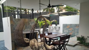 A hanging chair, a dining table, and chairs in a covered outdoor area with stone flooring and potted plants. - Charming 2-bedroom house in enjoyable Playa del Coco with WiFi, AC (Playa del Coco)