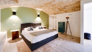 Een slaapkamer met een bakstenen plafond, een bed met donker hoofdeinde, nachtkastjes en een vloerlamp.