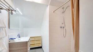 Een moderne badkamer met een witte wastafel, een houten kastje en een douche met een beige gordijn.