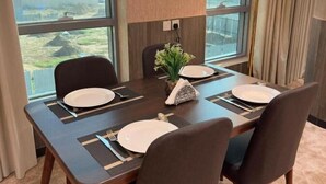 A dining area with a table set for four, large windows, and a lamp. - Ferbion hotel (Muhayil)