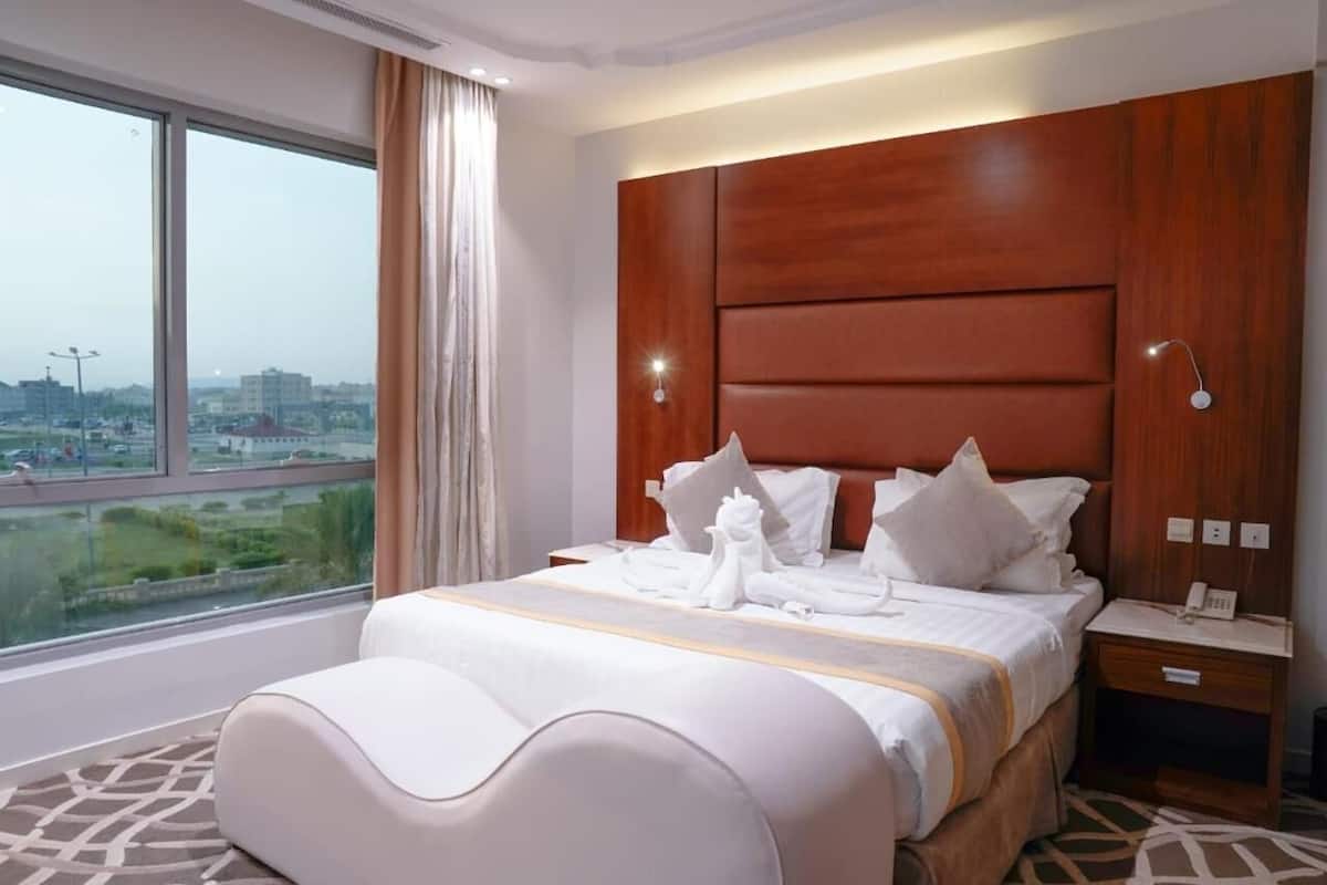 A hotel room with a large bed, a nightstand, a telephone, and a view of the city through a large window.