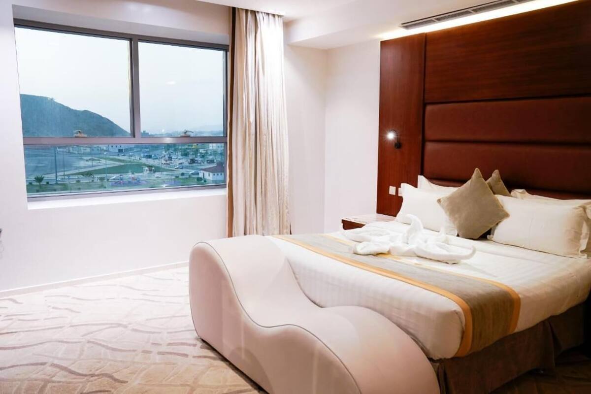 A hotel room with a large bed, a view of a cityscape through a window, and a wooden headboard.