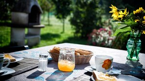 Un tavolo apparecchiato all'aperto, con un cesto di pane, un bicchiere di succo d'arancia, un saliera e una tazza decorata con un fiore.