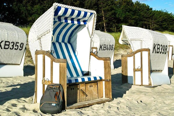 Beach chairs with white and blue striped covers, wooden frames, and a black bag on the sand.