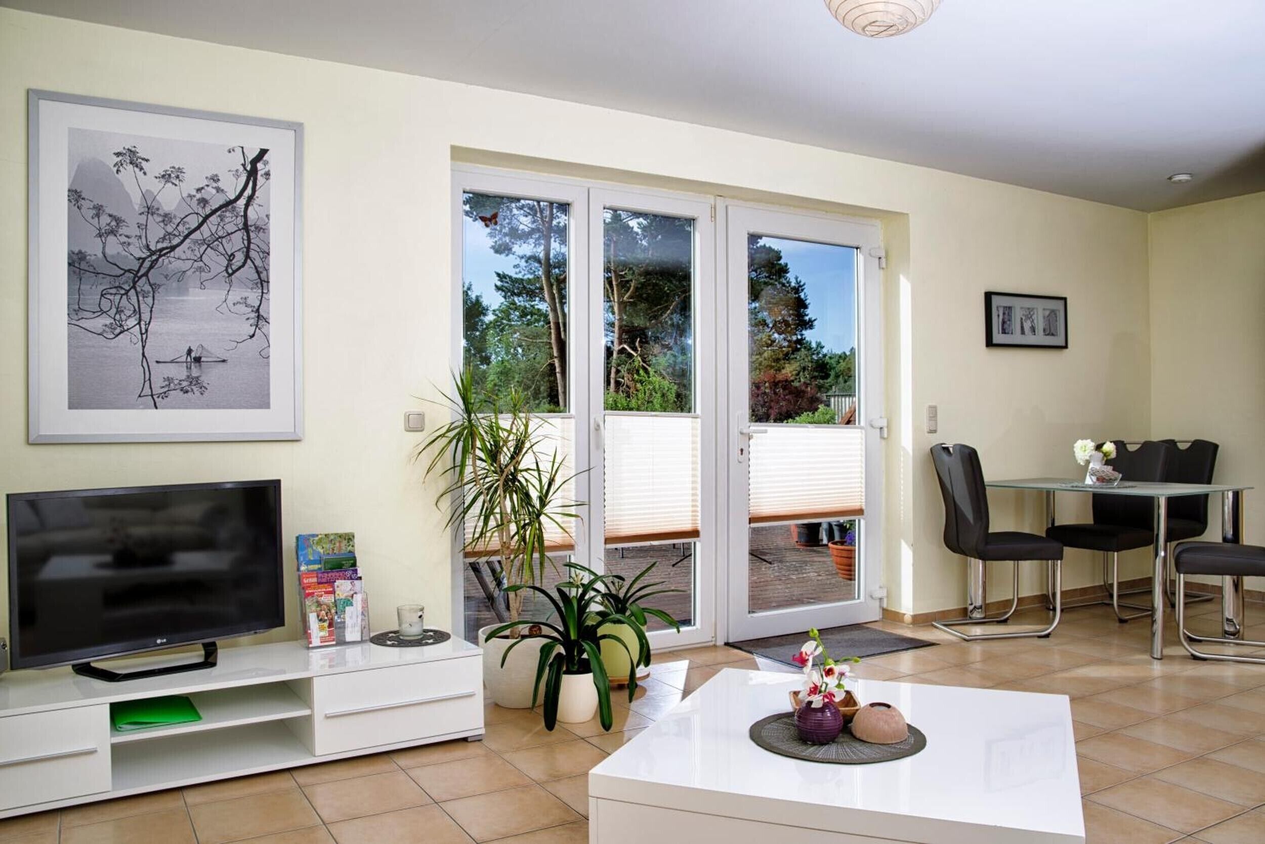 Una sala de estar con televisor, una mesa de comedor con sillas, un puerta corrediza de vidrio que da a un balcón, y un cuadro en la pared.