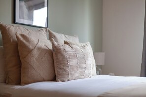 A neatly made bed with three beige pillows and a framed picture on the wall. - Trendy Flat in St Katharine (London)