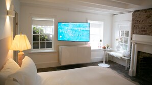 Habitació d'hotel amb llit, televisió penjada a la paret, làmpada, taula petita amb flors i una llar de foc.
