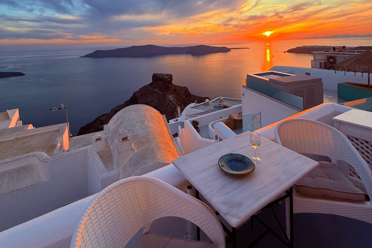 Una terrazza con mobili bianchi e un tavolo, con vista su un tramonto sul mare.