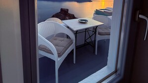 A balcony with a view of a sunset over water, white wicker furniture, and a table with a bowl. - Sunset Caldera Sea View Houses  (Santorini)