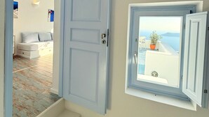 A room with a blue door, a small window with a view of the sea, and a staircase leading to another room. - Sunset Caldera Sea View Houses  (Santorini)