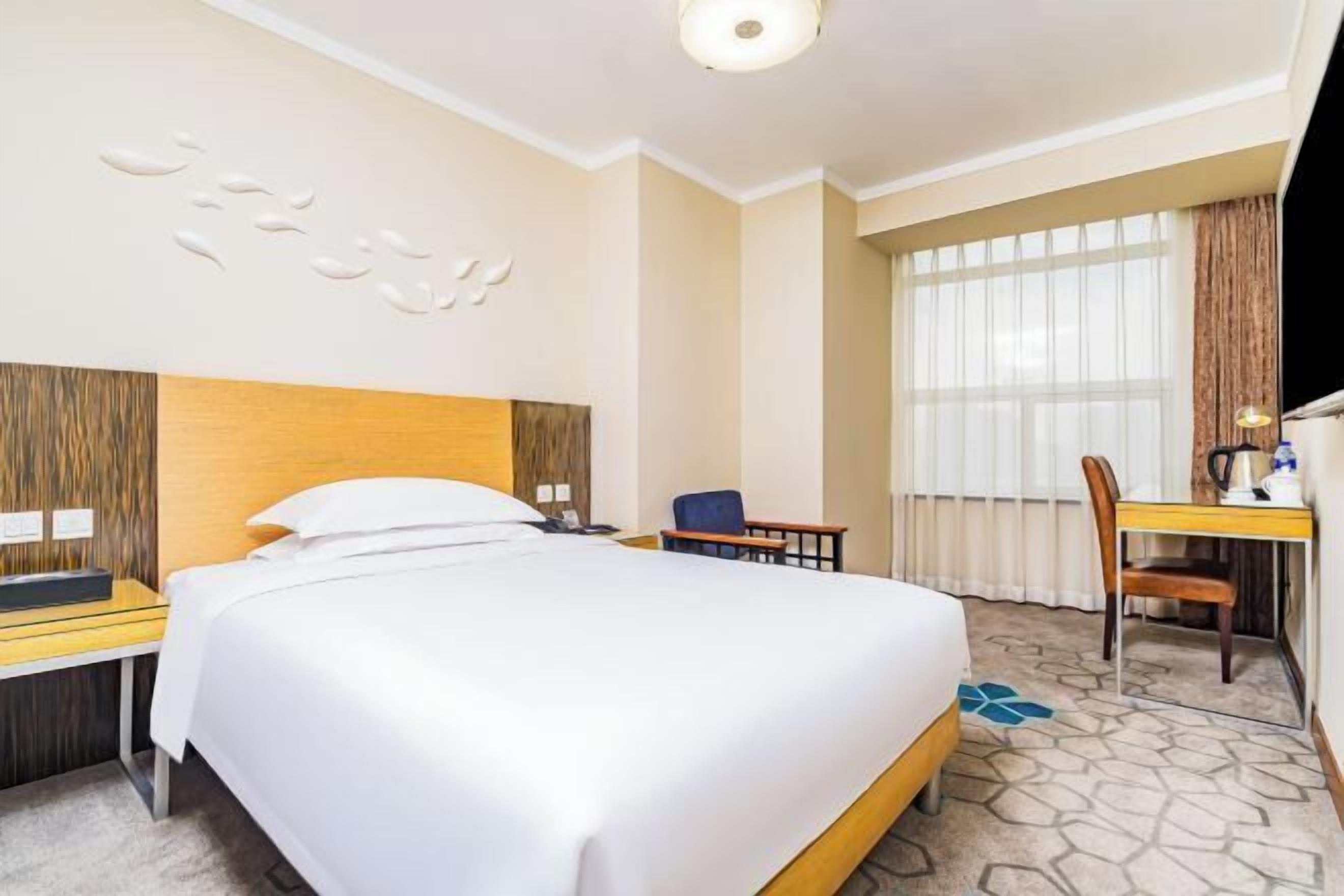 Une chambre d’hôtel avec un lit, un bureau, une chaise et une grande fenêtre.