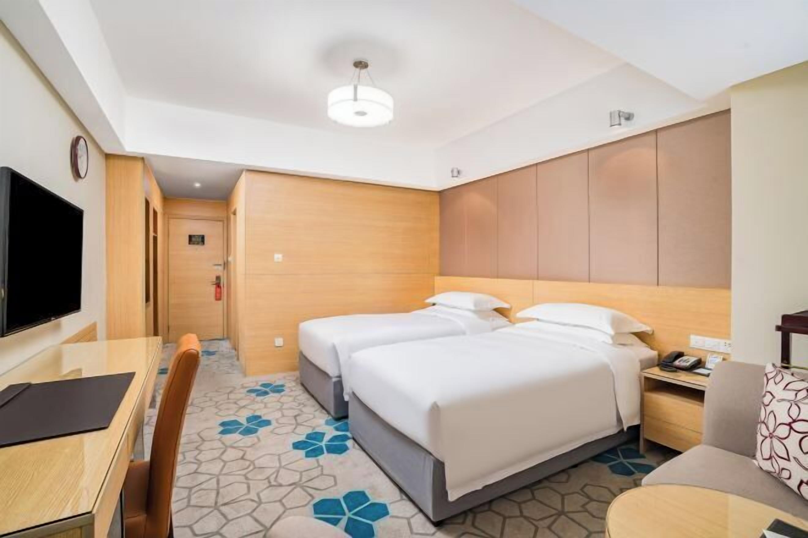 A hotel room with a bed, a desk, a chair, a television, and a clock.