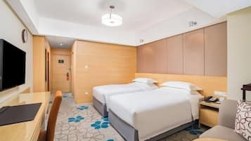 A hotel room with a bed, a desk, a chair, a television, and a clock.