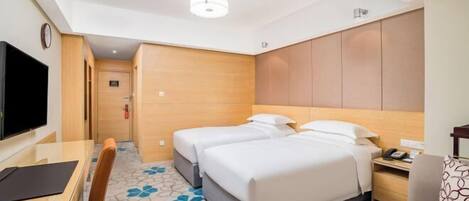 A hotel room with a bed, a desk, a chair, a television, and a clock.