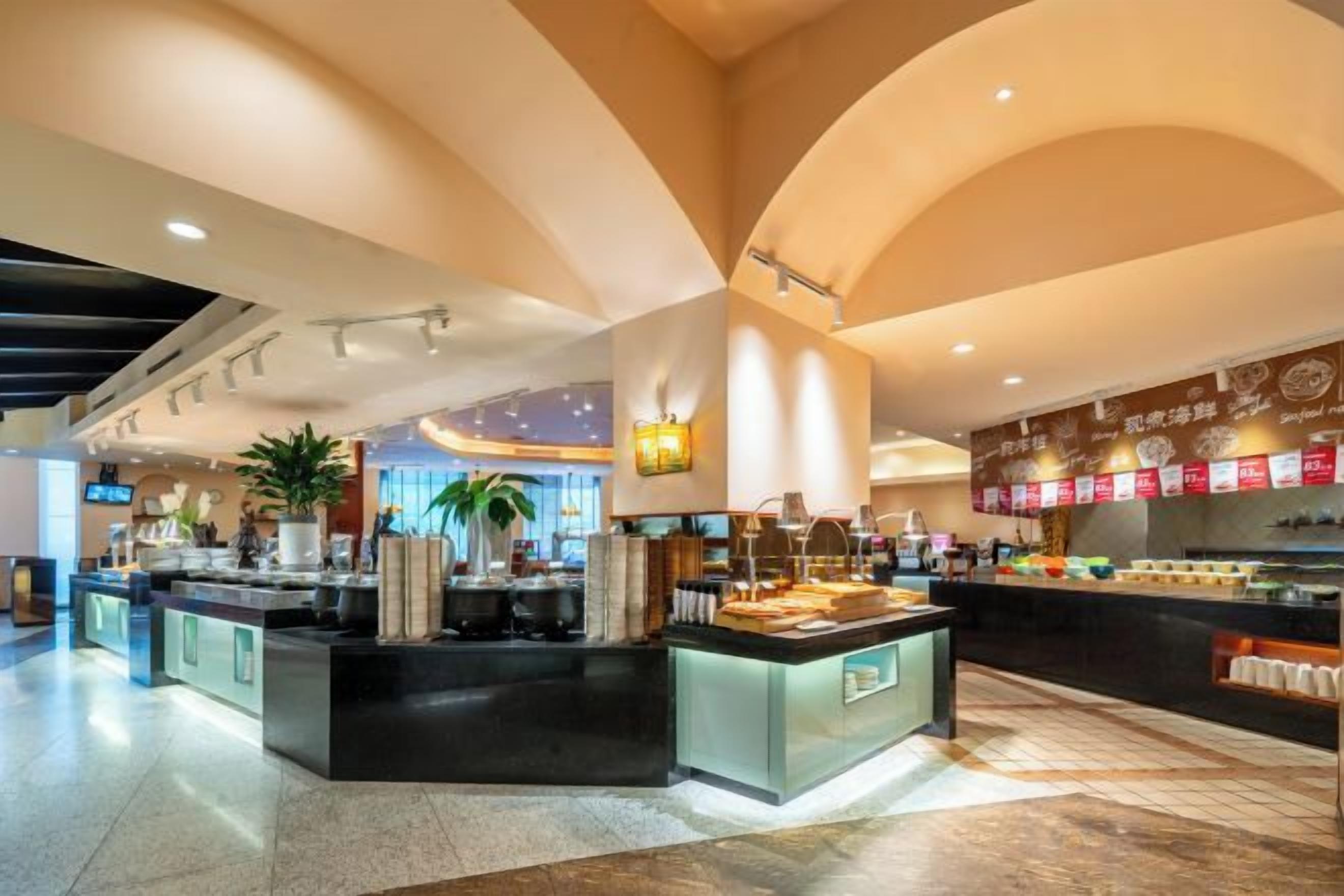 A modern hotel lobby with a central reception desk, a seating area, and a buffet counter.