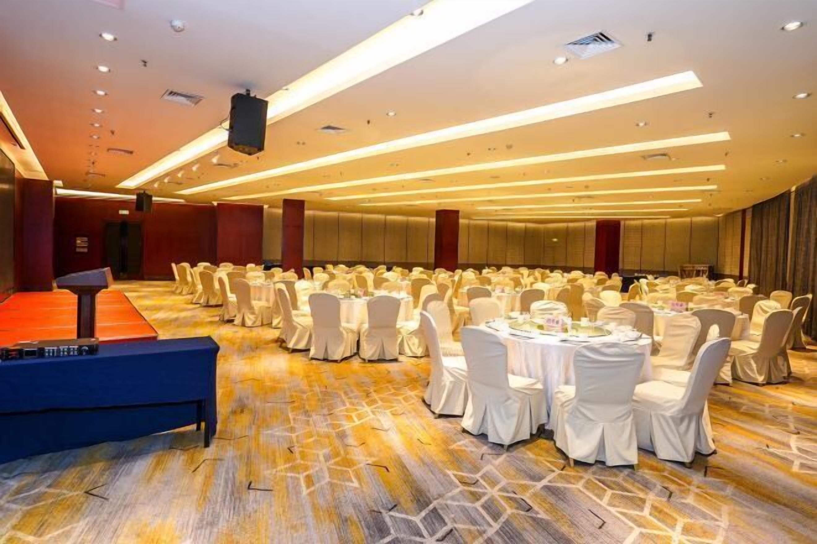 A banquet hall with round tables and chairs, a stage, and a carpeted floor.