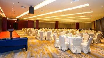 A banquet hall with round tables and chairs, a stage, and a carpeted floor.