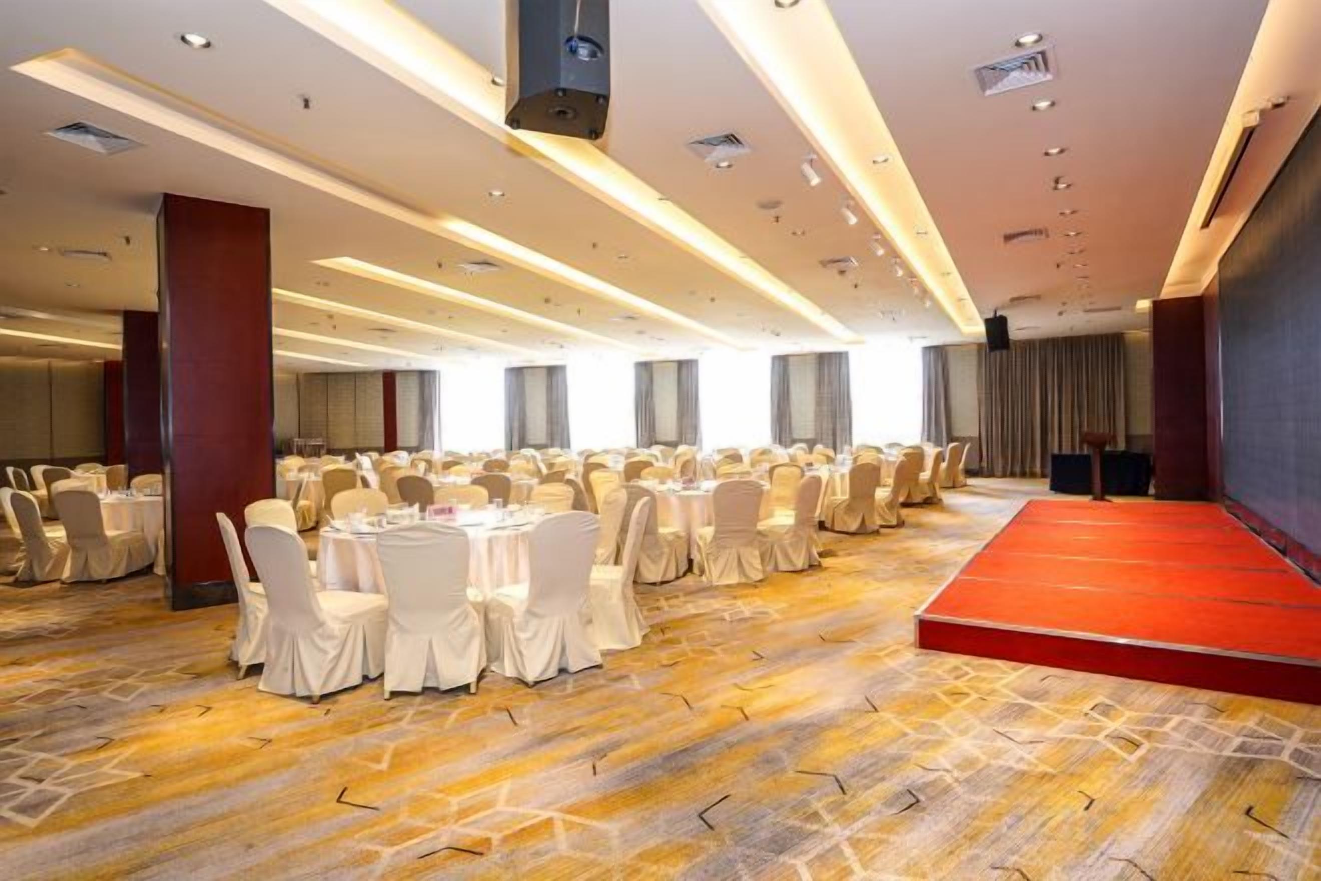 Un salón de banquetes con mesas redondas, un escenario y piso alfombrado.