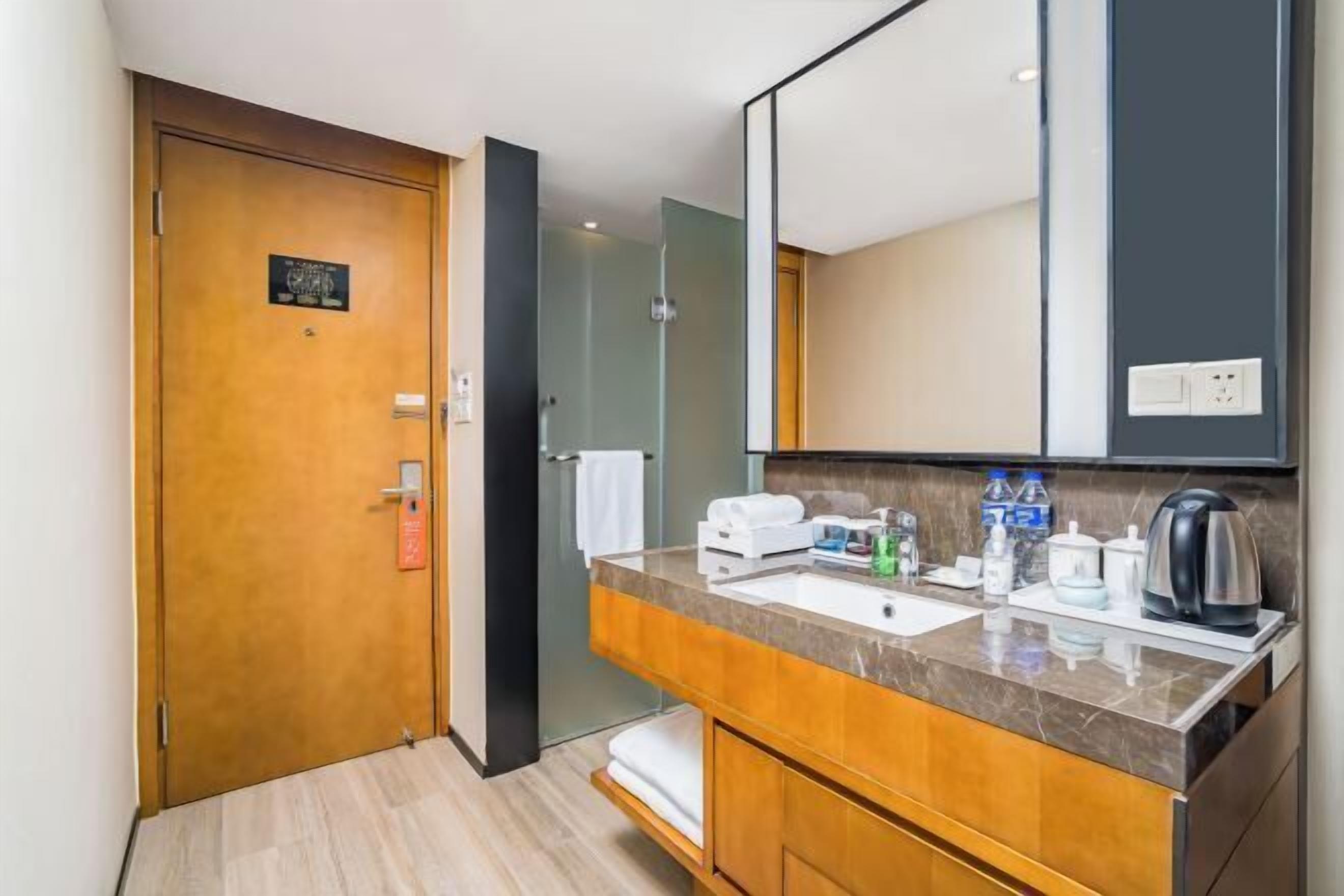 A hotel bathroom with a wooden door, a marble sink, a large mirror, and a towel rack.