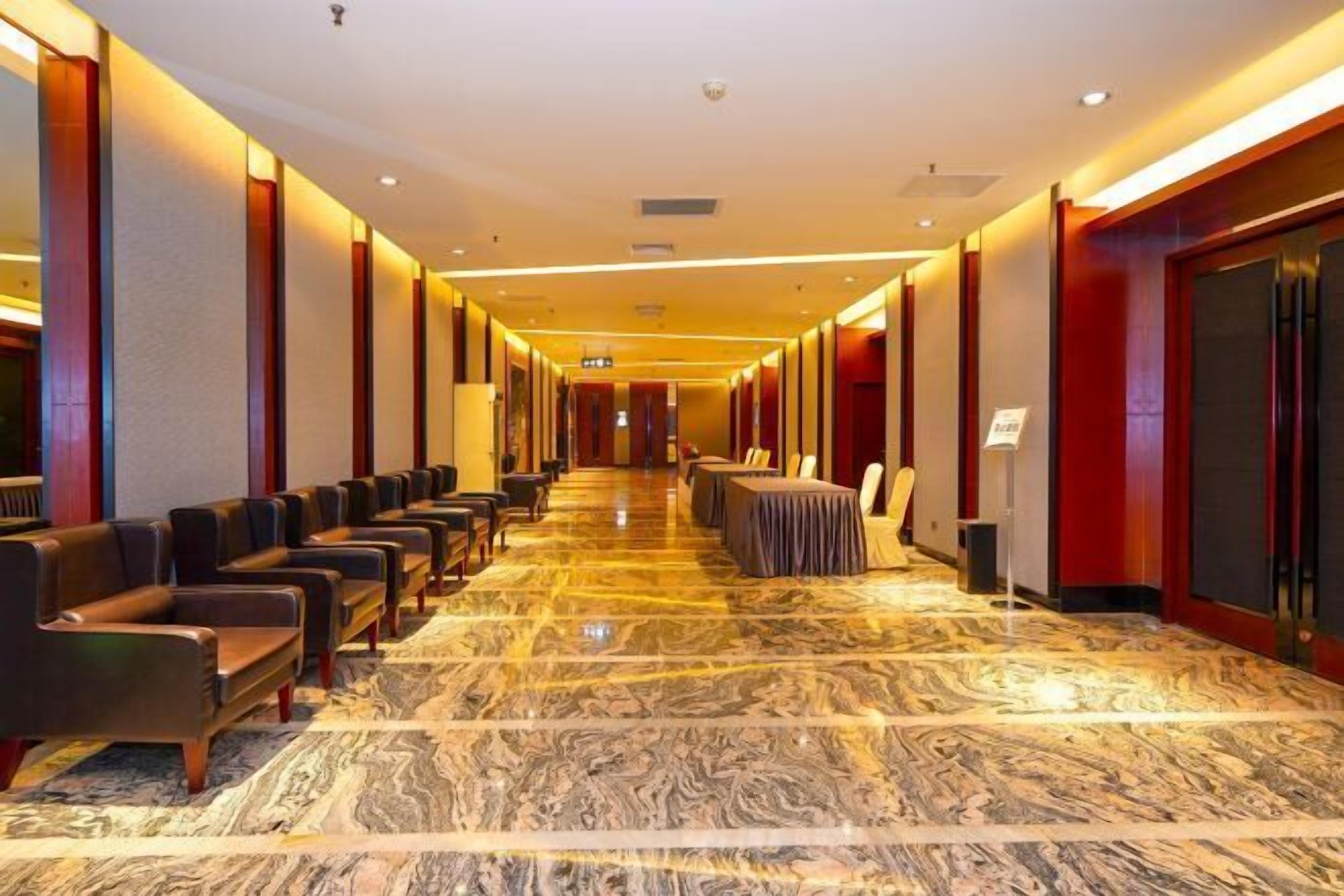 Ein Hotelgang mit Sitzreihen, einem Marmorboden und einer roten Akzentwand.
