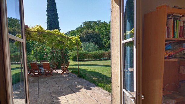 A patio area with a table and chairs, a pergola with climbing plants, and a view of a garden with a tall tree. - Provencal house with pool and garden in the Aix countryside (puyricard)