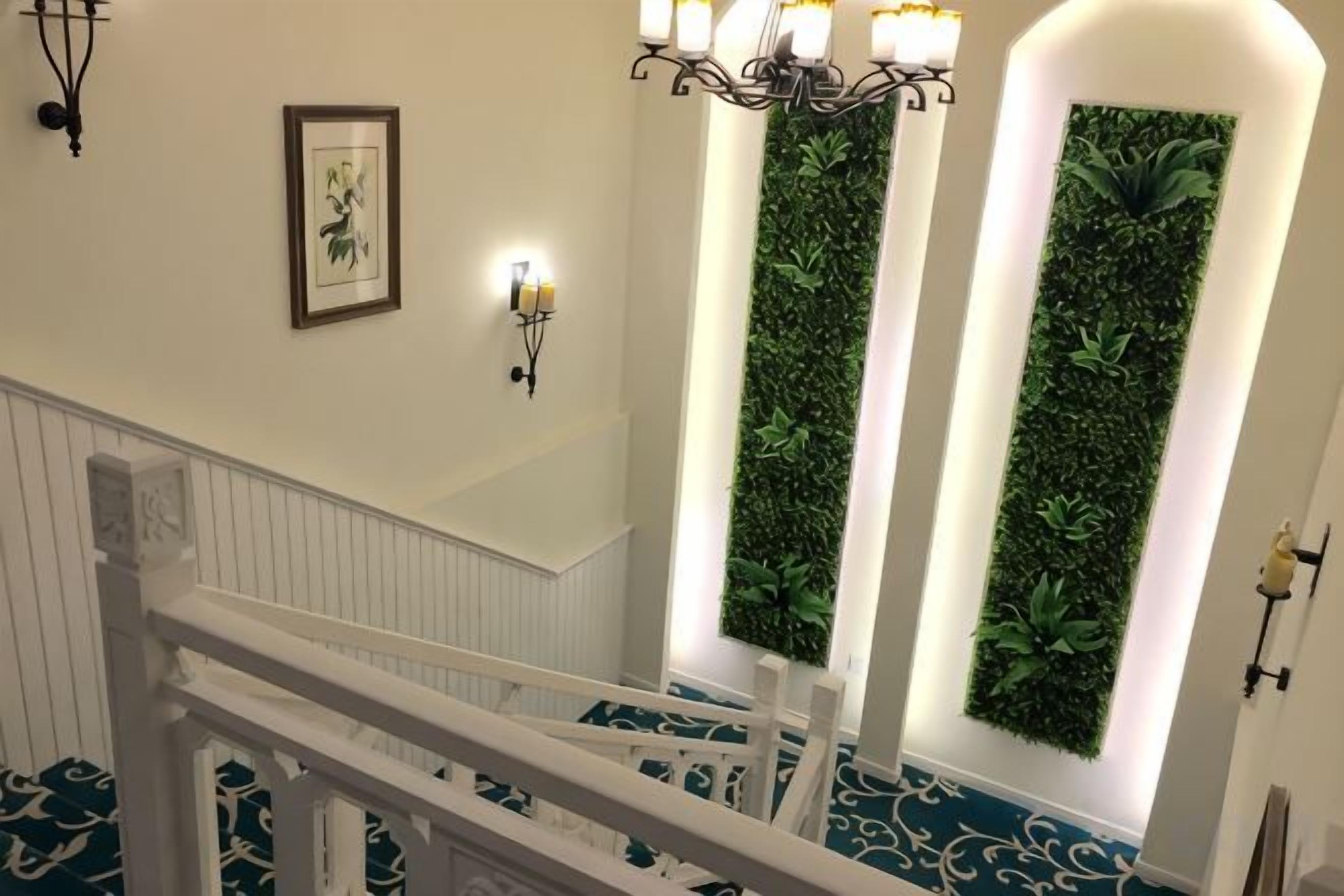 Escadaria com corrimão branco, luminária fixada na parede e painel de jardim vertical.