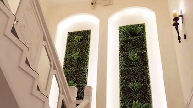 Un escalier avec des rampes blanches et un mur orné d’installations végétales verticales.