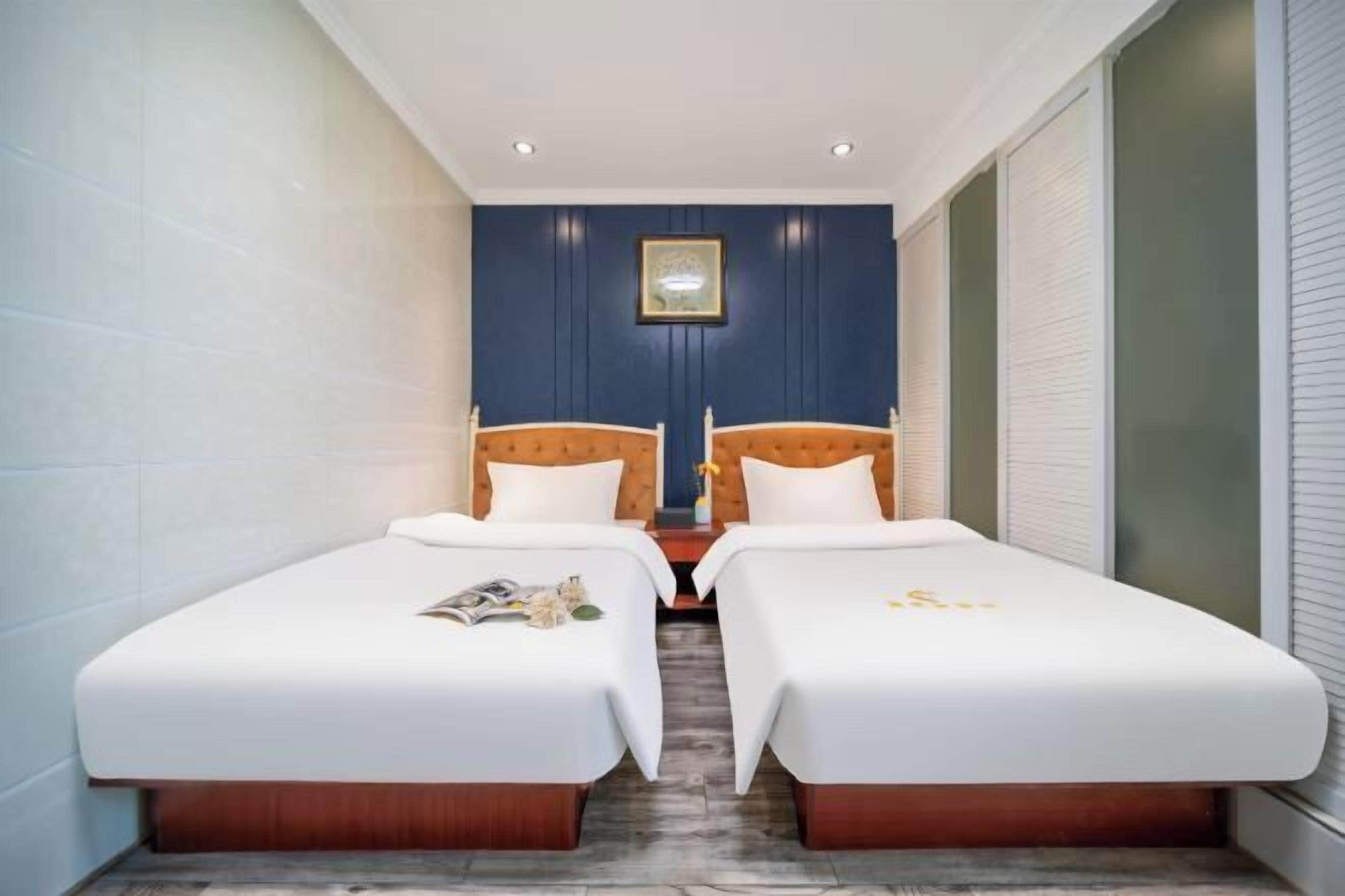 Quarto de hotel com duas camas de solteiro, uma mesa pequena e um quadro pendurado na parede.