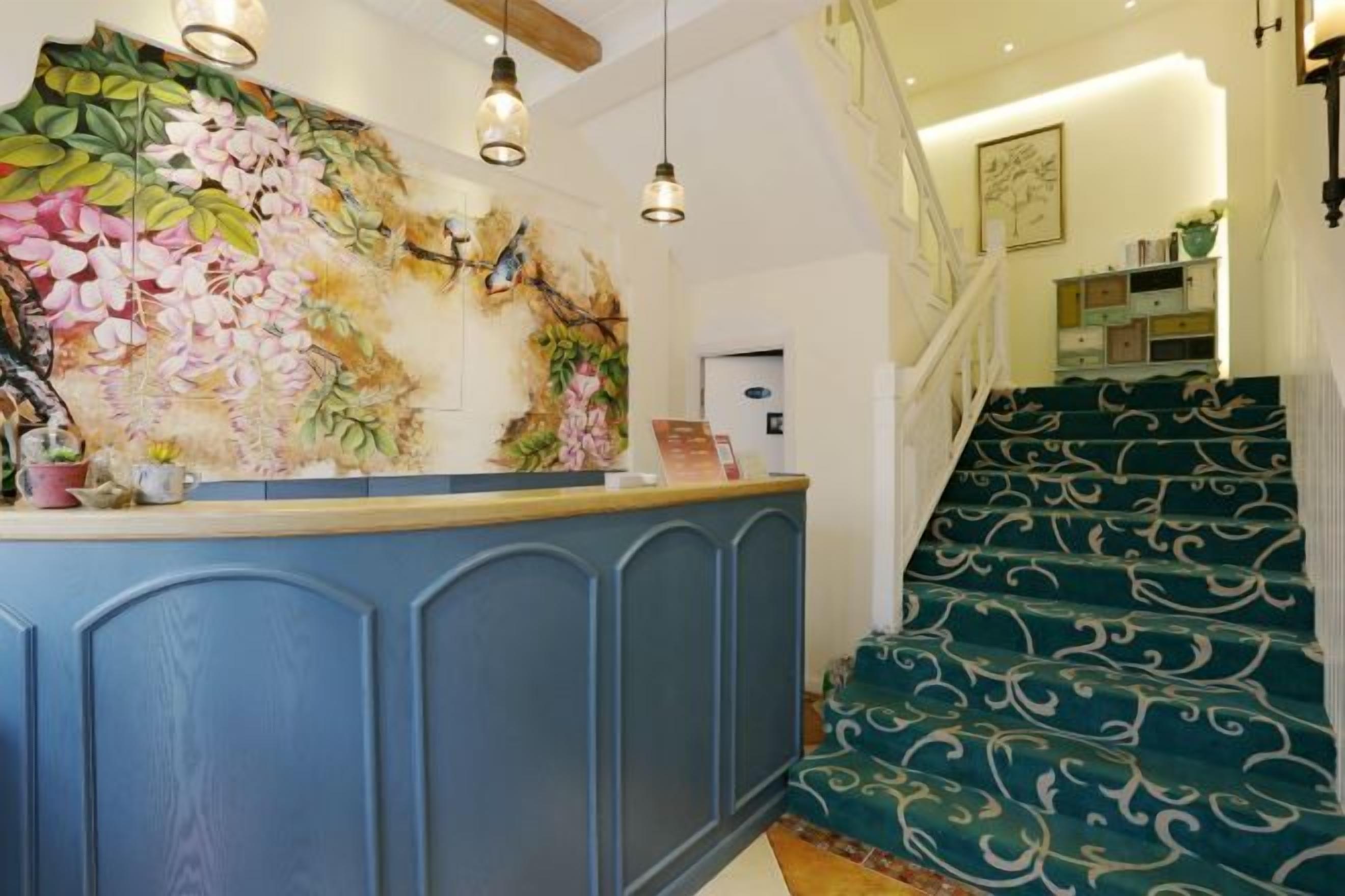 A reception area with a blue counter, a floral mural, and a staircase with patterned carpet.