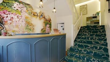 A reception area with a blue counter, a floral mural, and a staircase with patterned carpet.