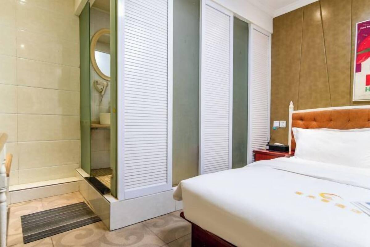 A hotel room with a bed, a nightstand, a mirror, and a shower area.