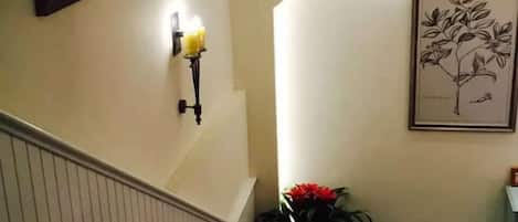 A staircase with a wall-mounted light fixture and a framed botanical illustration.