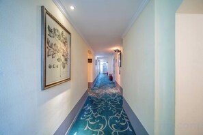 A hallway with a patterned carpet, framed artwork on the wall, and a fire extinguisher.