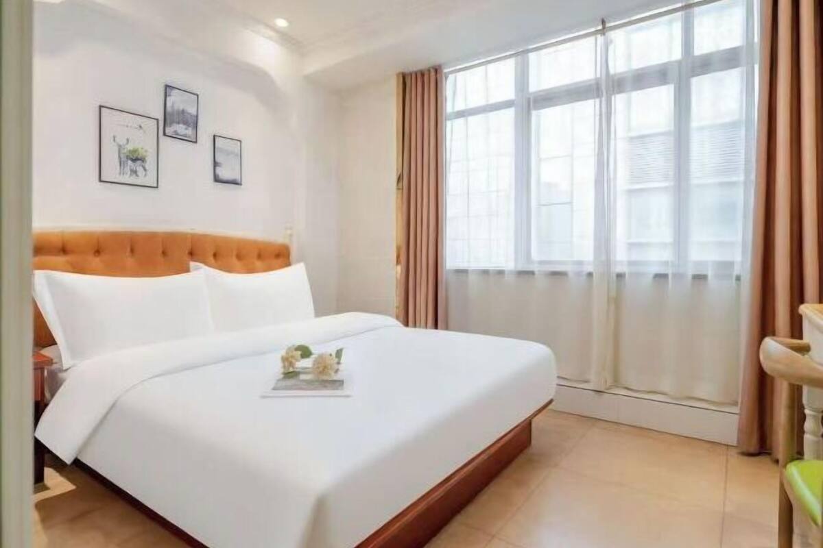 A hotel room with a bed, a window with curtains, and wall art.