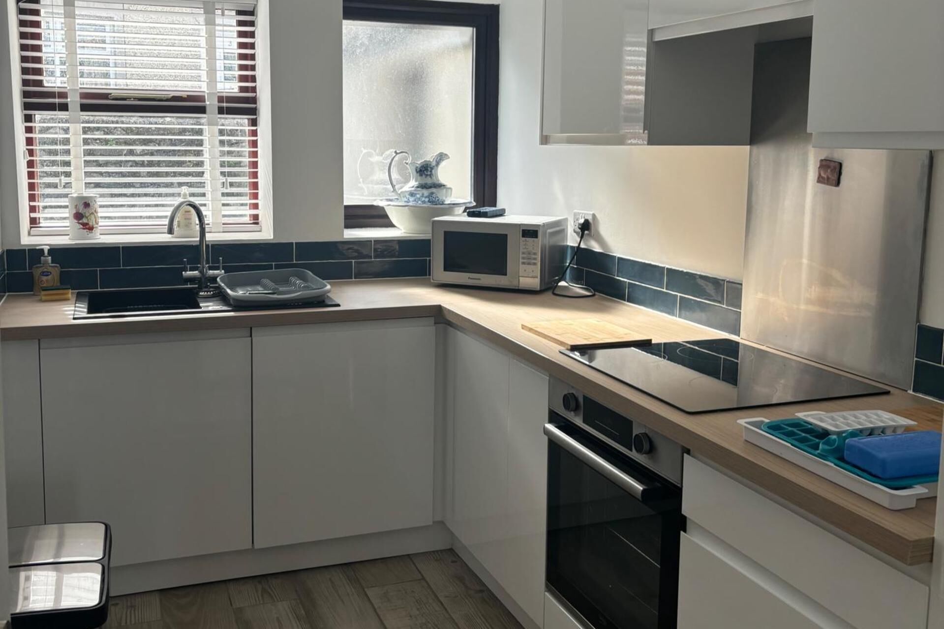 A modern kitchen with white cabinets, a stainless steel refrigerator, a microwave, and a sink with a window above it.